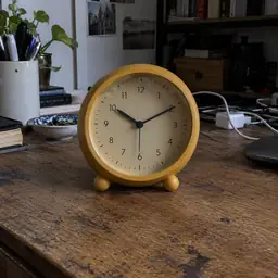round ochre analog table clock on two small feet, as photographed