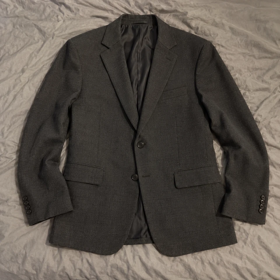 charcoal tailored single-breasted blazer with two black buttons and notch lapels, laid flat on a bed