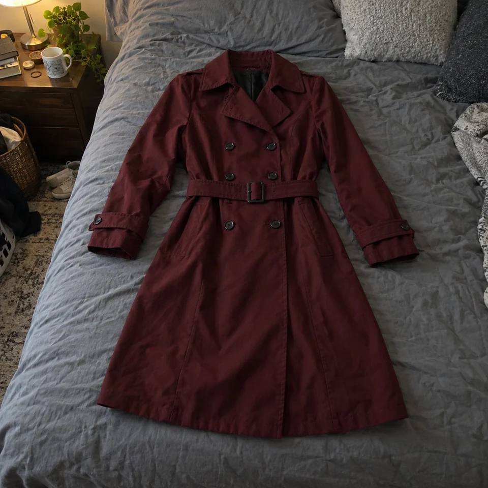 deep burgundy double-breasted trench coat with belt and six front buttons, laid flat on a bed