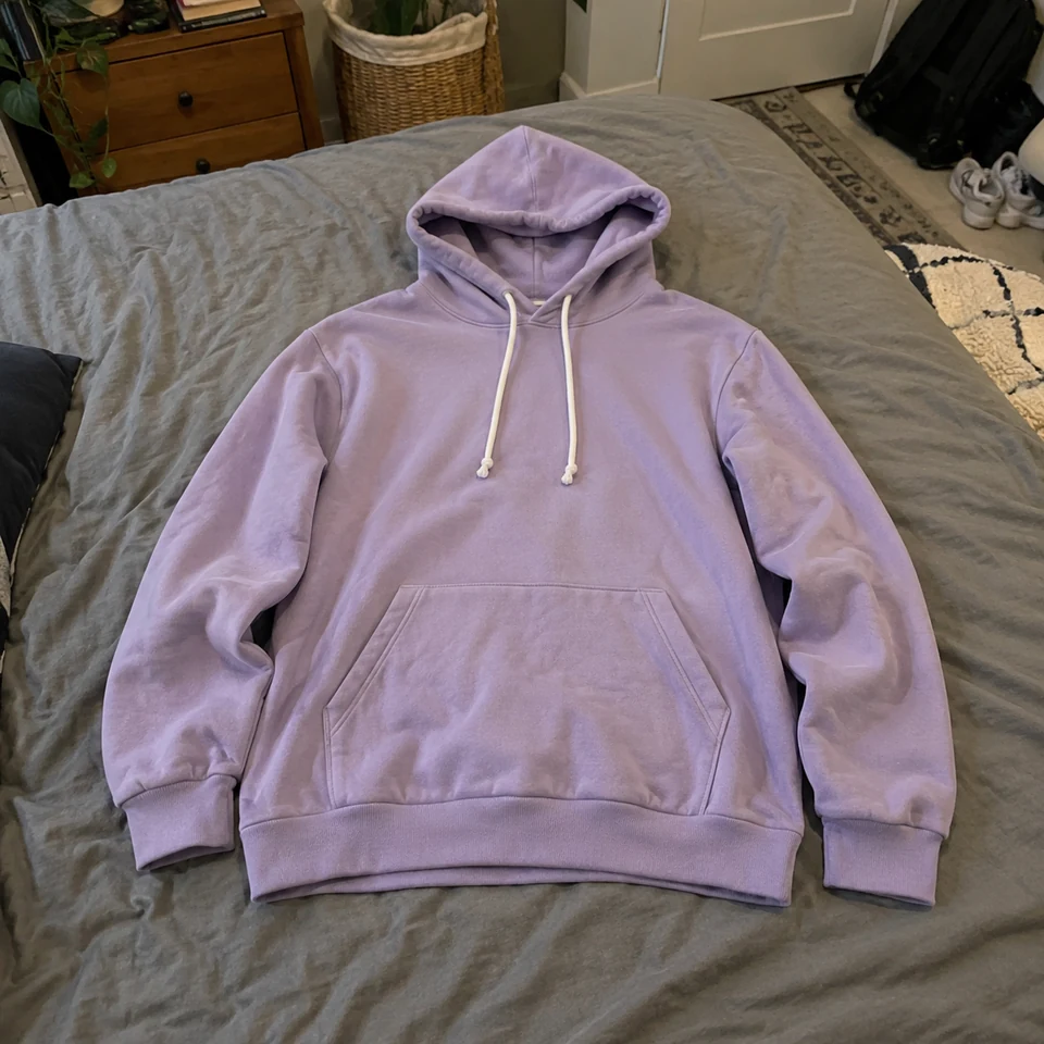 plain lavender pullover hoodie with kangaroo pocket and white drawstrings, laid flat on a bed