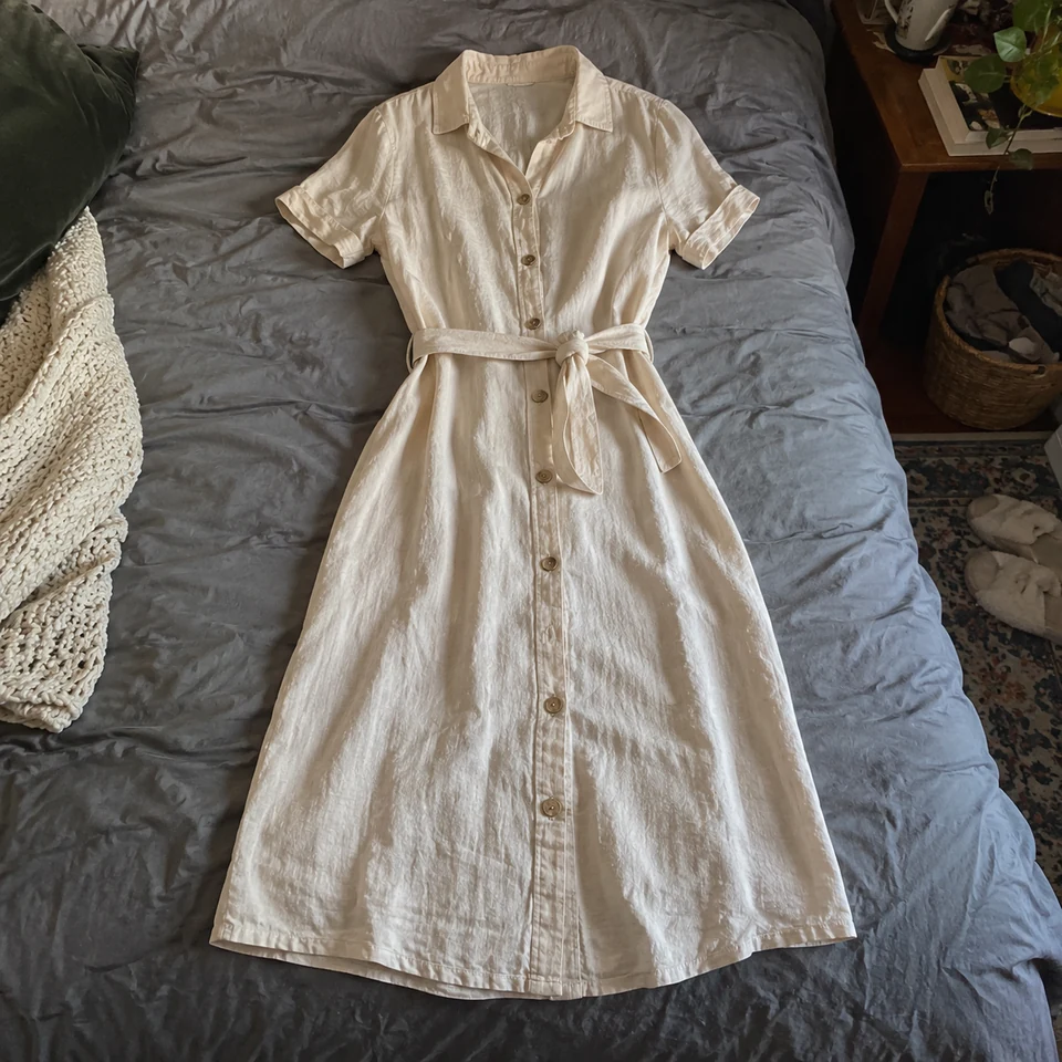 warm ivory linen midi dress with short sleeves and fabric belt, laid flat on a bed