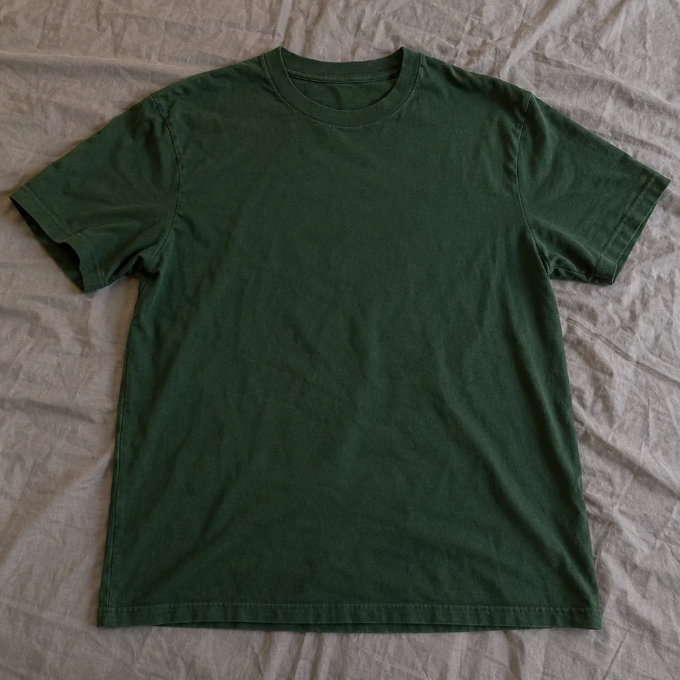 forest-green plain cotton crewneck short-sleeve T-shirt, laid flat on a bed