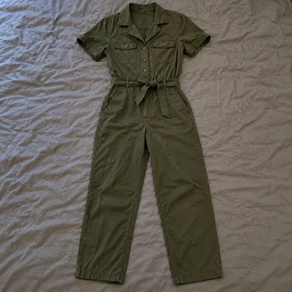 dark olive utility jumpsuit with short sleeves, buttons and belt, laid flat on a bed
