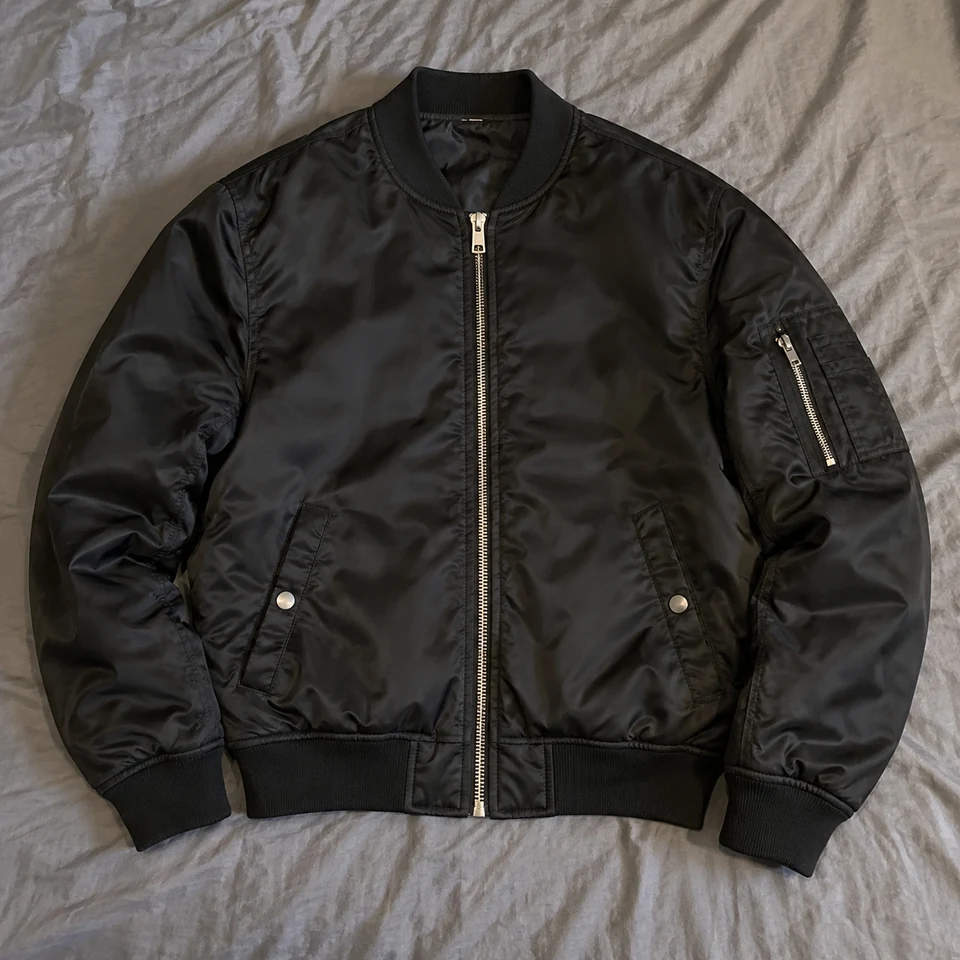 black satin bomber jacket with ribbed cuffs and front silver zipper, laid flat on a bed