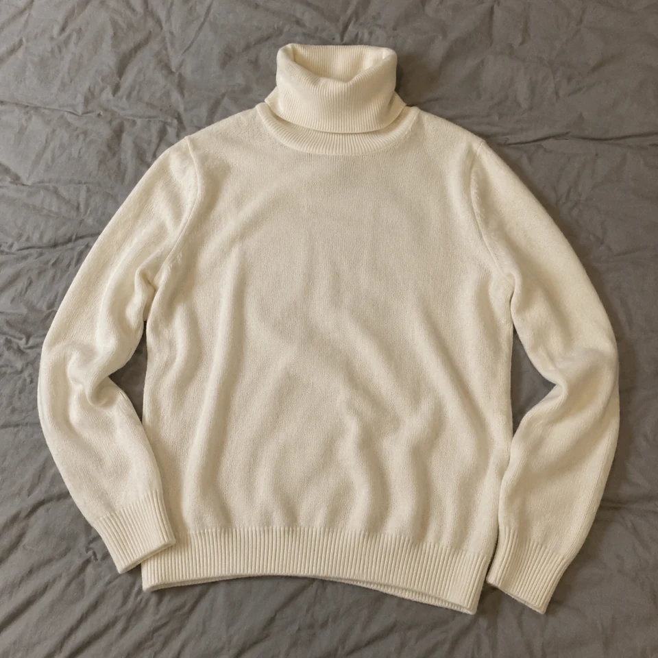 ivory fine-knit long-sleeve turtleneck sweater, laid flat on a bed