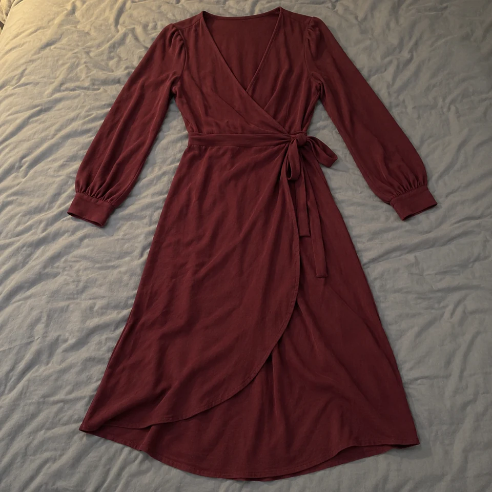 burgundy wrap midi dress with long sleeves and side waist tie, laid flat on a bed