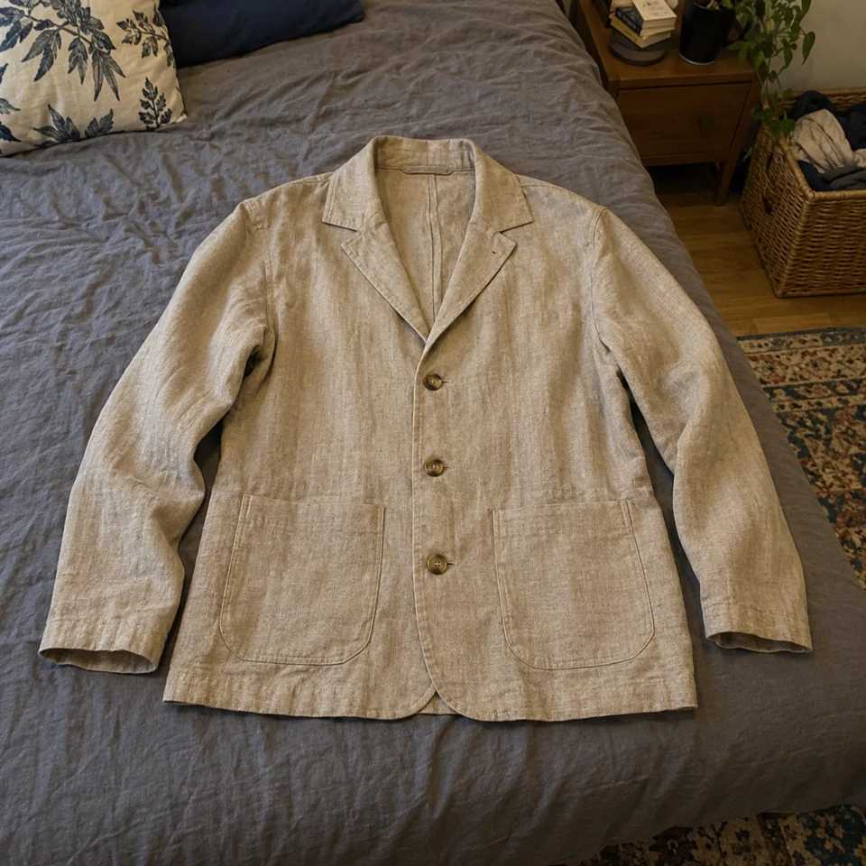sand linen lightweight jacket with patch pockets and three buttons, laid flat on a bed
